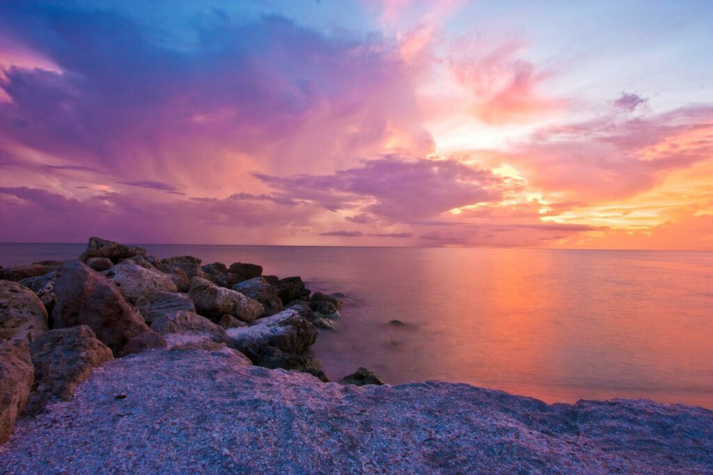 sunrise sky of blue, orange, pink and purple over the ocean with rocks to the left