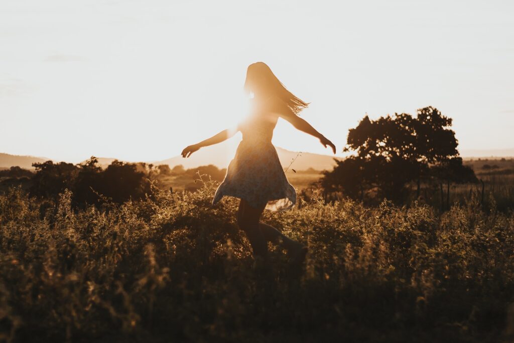 woman in a dress twirling in a filed as the sun goes down