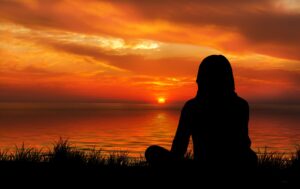 woman sitting on the beach watching the sun set over the ocean 